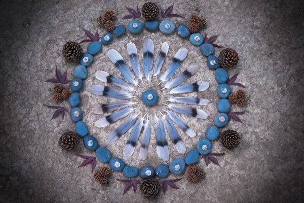 A sunburst altar of blue feathers, stones, and pinecones