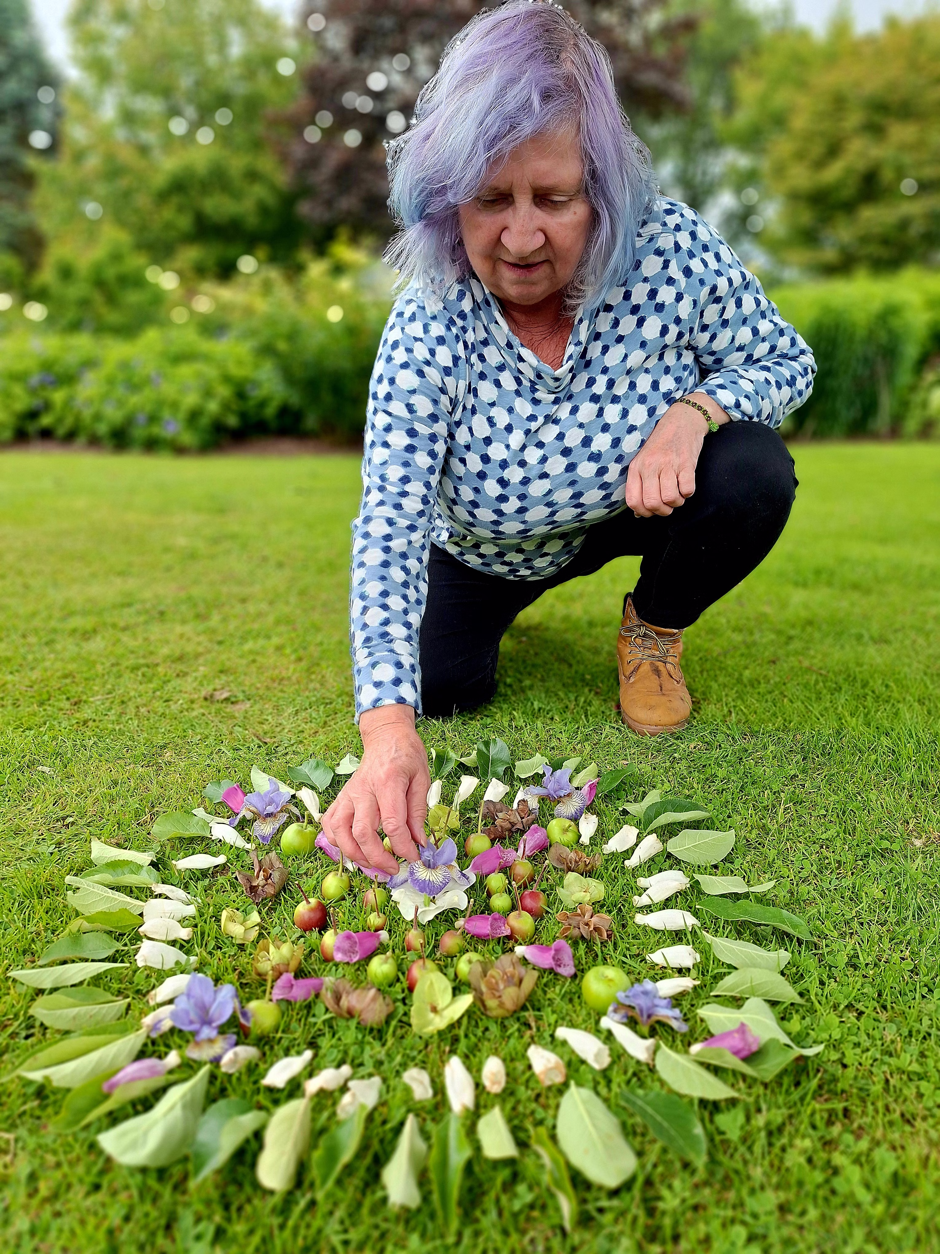 A woman crouched over a flower altar she's building on a garden lawn